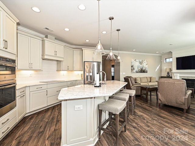 kitchen featuring appliances with stainless steel finishes, light stone counters, dark hardwood / wood-style floors, hanging light fixtures, and an island with sink