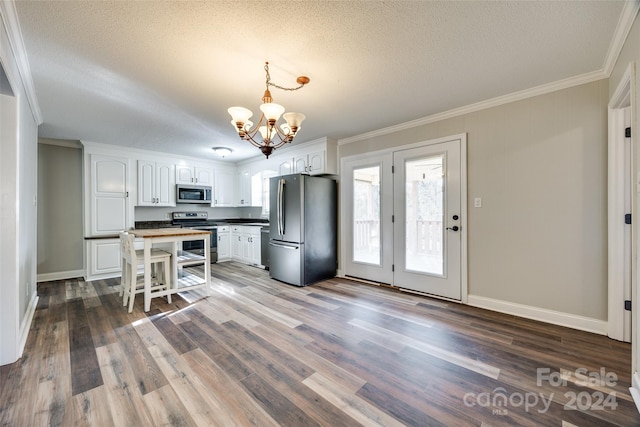 kitchen with white cabinets, hardwood / wood-style flooring, ornamental molding, appliances with stainless steel finishes, and decorative light fixtures