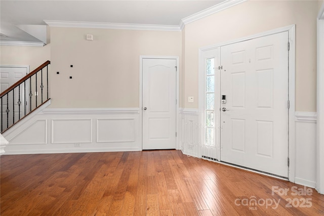 entryway featuring ornamental molding, wood-type flooring, a wainscoted wall, and stairs