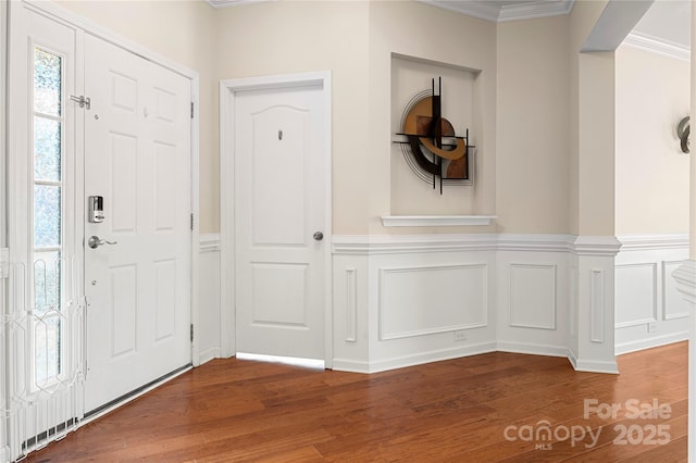 foyer entrance with ornamental molding, wainscoting, wood finished floors, and a decorative wall