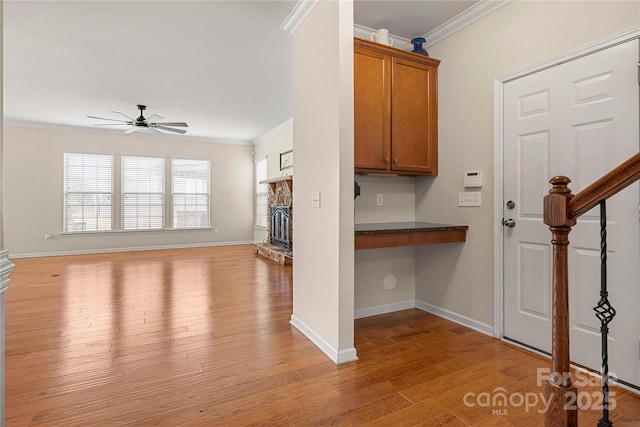 interior space with a stone fireplace, light wood-style floors, ornamental molding, brown cabinetry, and dark countertops