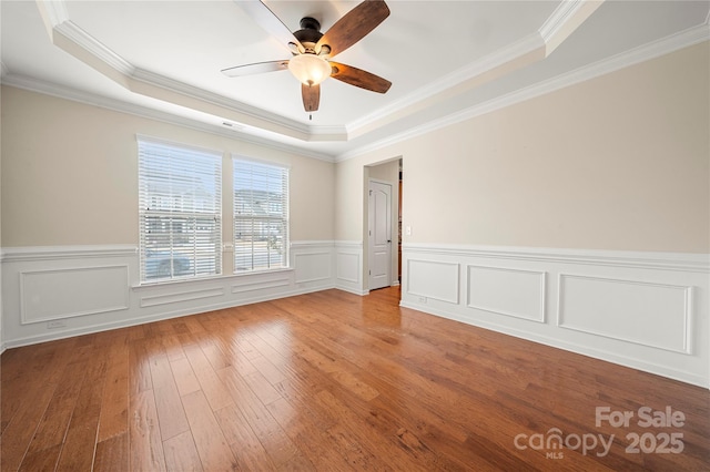 unfurnished room with ceiling fan, ornamental molding, a raised ceiling, and light wood-style floors