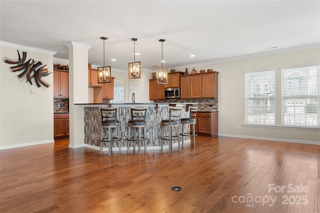 kitchen with dark wood-style floors, a breakfast bar area, tasteful backsplash, stainless steel microwave, and brown cabinetry