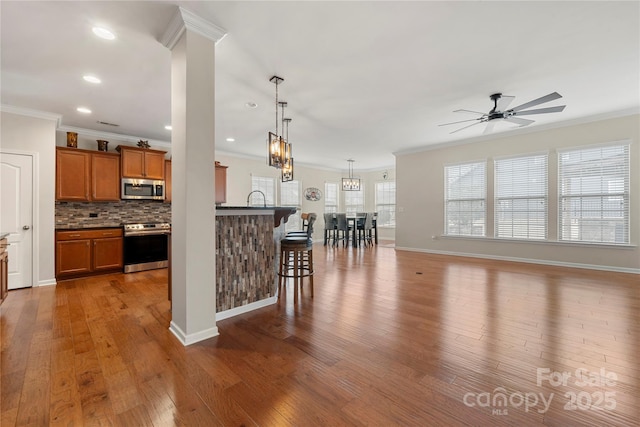 kitchen with stainless steel appliances, wood finished floors, a kitchen breakfast bar, backsplash, and brown cabinets