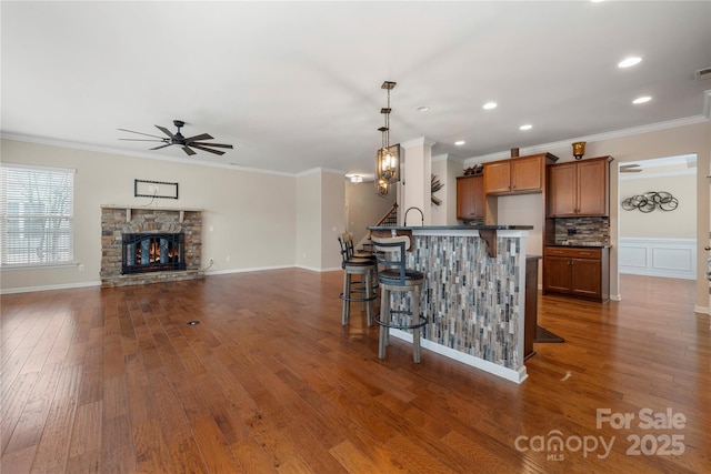 kitchen with dark wood-style floors, a fireplace, dark countertops, brown cabinetry, and a kitchen breakfast bar