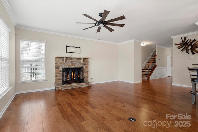 unfurnished living room featuring a ceiling fan, stairway, hardwood / wood-style floors, crown molding, and a stone fireplace