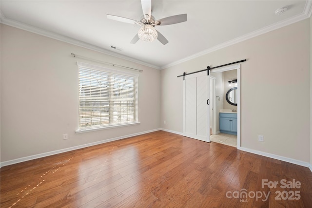 unfurnished bedroom featuring ornamental molding, wood-type flooring, and a barn door