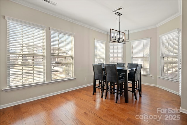 dining room with a chandelier, hardwood / wood-style flooring, visible vents, a healthy amount of sunlight, and ornamental molding