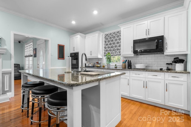 kitchen featuring a center island with sink, white cabinetry, dark stone countertops, and black appliances