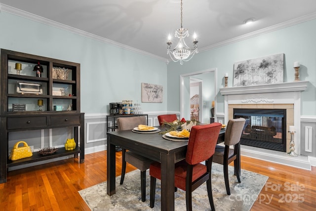 dining room with a tile fireplace, wood-type flooring, a notable chandelier, and ornamental molding