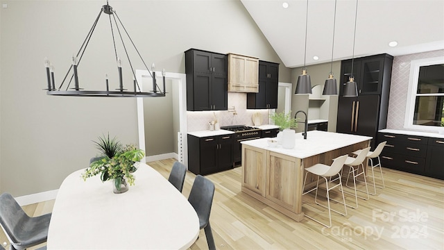 kitchen featuring a center island with sink, an inviting chandelier, a kitchen breakfast bar, pendant lighting, and light hardwood / wood-style flooring