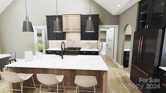 kitchen featuring a center island with sink, refrigerator, tasteful backsplash, high vaulted ceiling, and decorative light fixtures