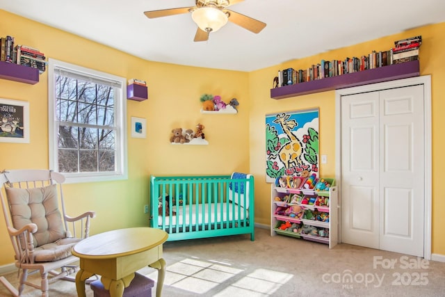 bedroom with a nursery area, carpet, ceiling fan, and a closet