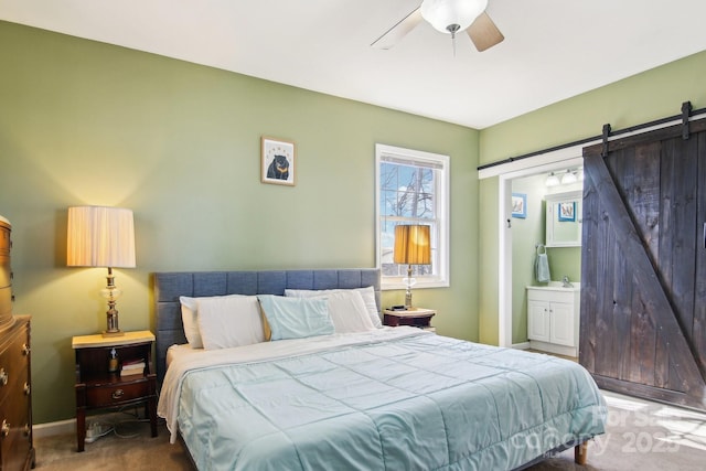 bedroom featuring ceiling fan, connected bathroom, a barn door, and carpet floors