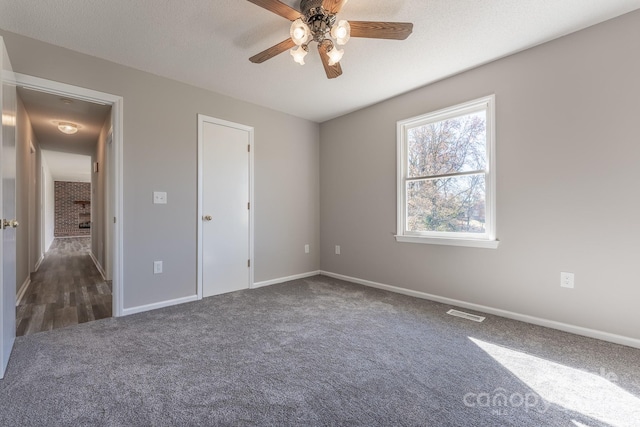 unfurnished bedroom featuring ceiling fan, dark carpet, and a textured ceiling