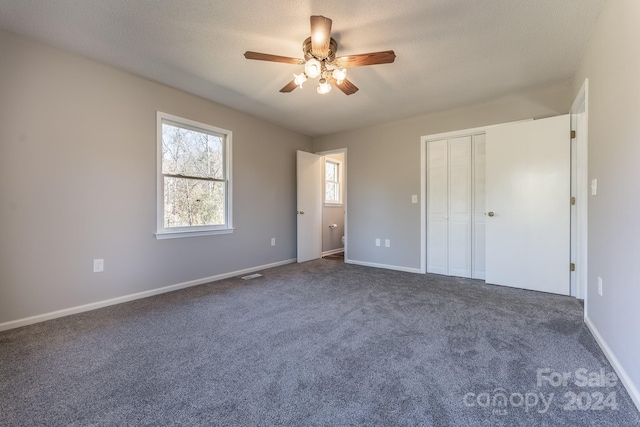 unfurnished bedroom featuring dark colored carpet, a textured ceiling, a closet, and ceiling fan