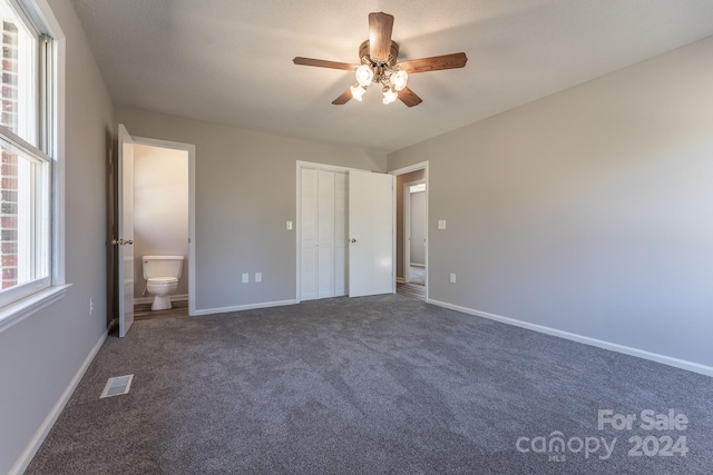 unfurnished bedroom featuring ceiling fan, dark carpet, a closet, and ensuite bath