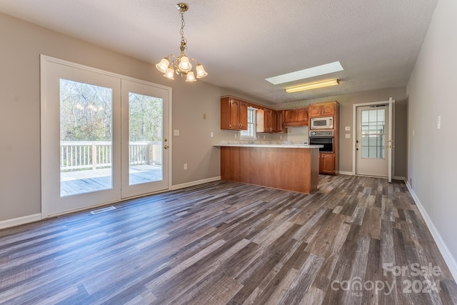 kitchen with a skylight, dark wood-type flooring, kitchen peninsula, black oven, and white microwave