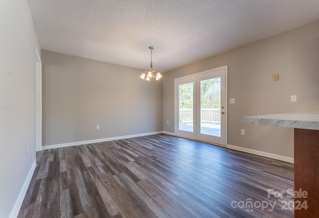 empty room featuring dark wood-type flooring, a textured ceiling, and a notable chandelier