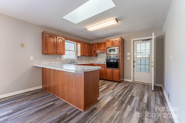 kitchen featuring stainless steel microwave, dark wood-type flooring, oven, a skylight, and kitchen peninsula