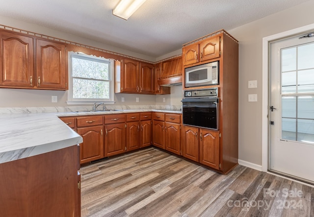 kitchen with stainless steel microwave, oven, sink, a textured ceiling, and light hardwood / wood-style floors