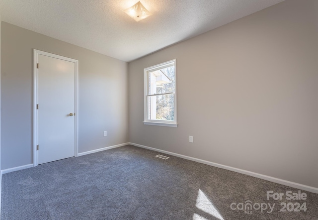 empty room featuring dark carpet and a textured ceiling