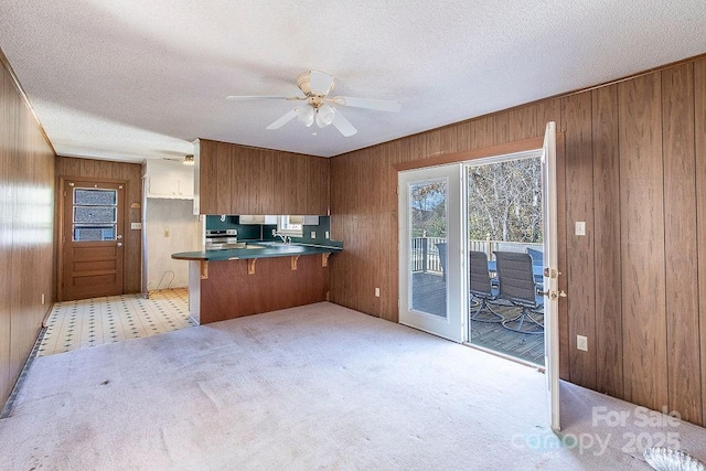 kitchen featuring ceiling fan, a textured ceiling, wooden walls, and kitchen peninsula