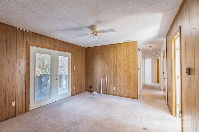 spare room featuring light colored carpet, wood walls, and french doors