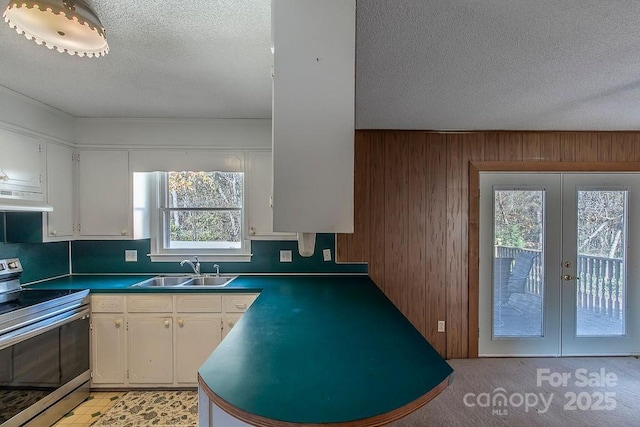 kitchen featuring stainless steel range with electric stovetop, wood walls, sink, and white cabinets