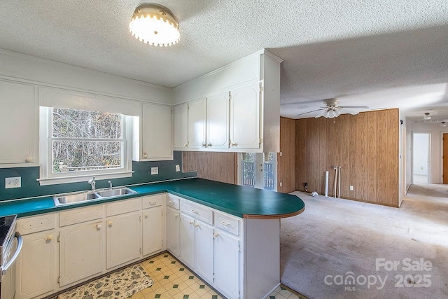 kitchen featuring sink, a textured ceiling, wooden walls, kitchen peninsula, and white cabinets