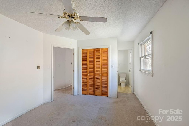 unfurnished bedroom featuring connected bathroom, light colored carpet, ceiling fan, a textured ceiling, and a closet