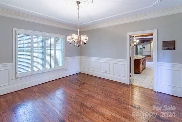 unfurnished dining area featuring hardwood / wood-style flooring, crown molding, and a notable chandelier