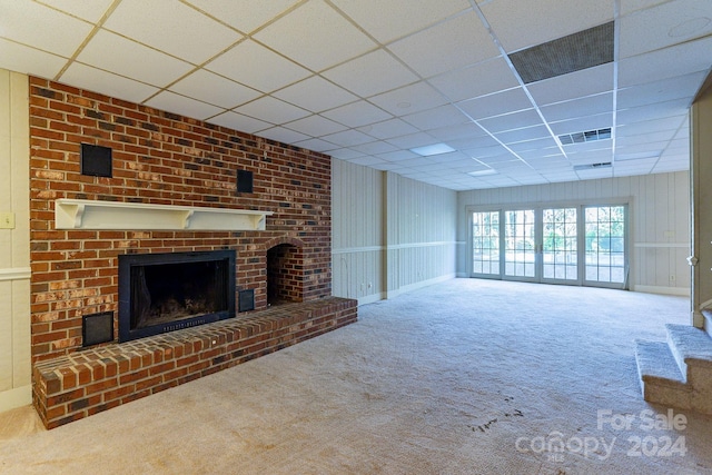 unfurnished living room featuring carpet floors, a brick fireplace, and a drop ceiling