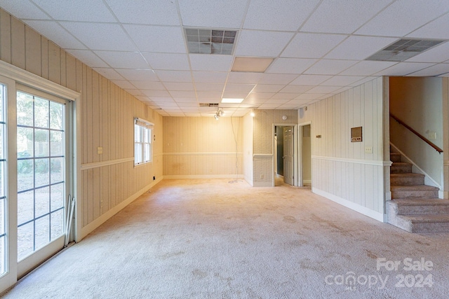 unfurnished room featuring carpet, a drop ceiling, and wood walls