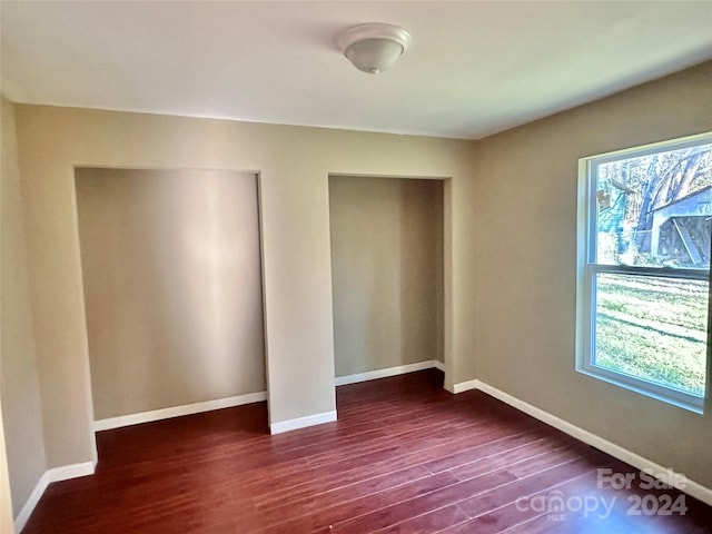 unfurnished bedroom featuring dark wood-type flooring and two closets