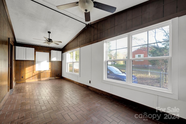 unfurnished room with wooden walls, ceiling fan, and vaulted ceiling