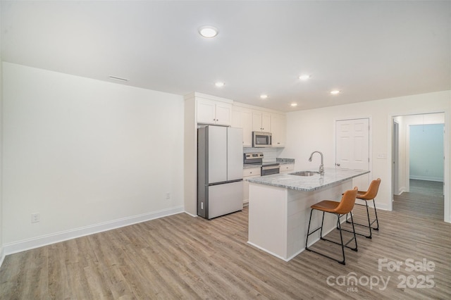 kitchen featuring light stone counters, a sink, white cabinetry, appliances with stainless steel finishes, and a center island with sink