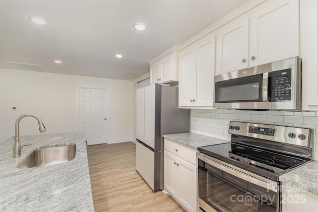 kitchen featuring light stone counters, light wood-style flooring, stainless steel appliances, a sink, and white cabinets