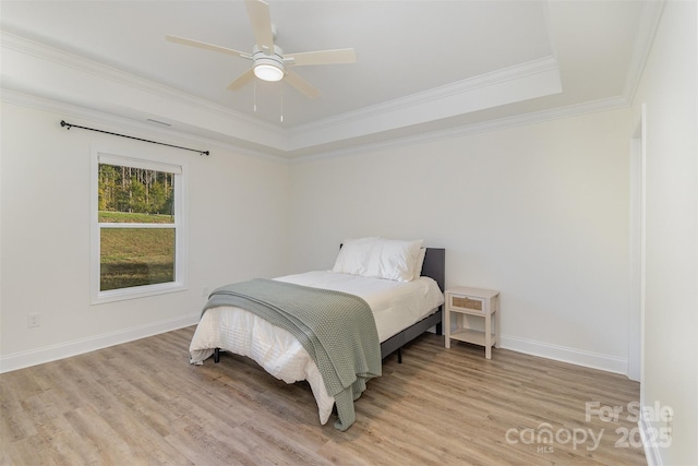 bedroom featuring baseboards, light wood-style flooring, ceiling fan, a tray ceiling, and crown molding