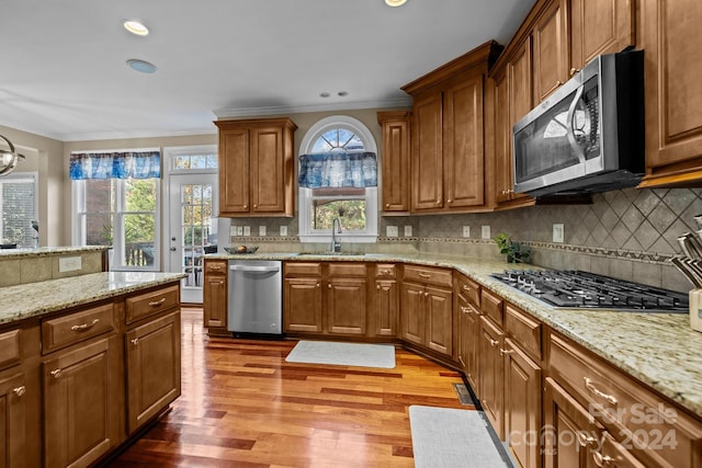 kitchen with light stone countertops, appliances with stainless steel finishes, tasteful backsplash, sink, and hardwood / wood-style flooring