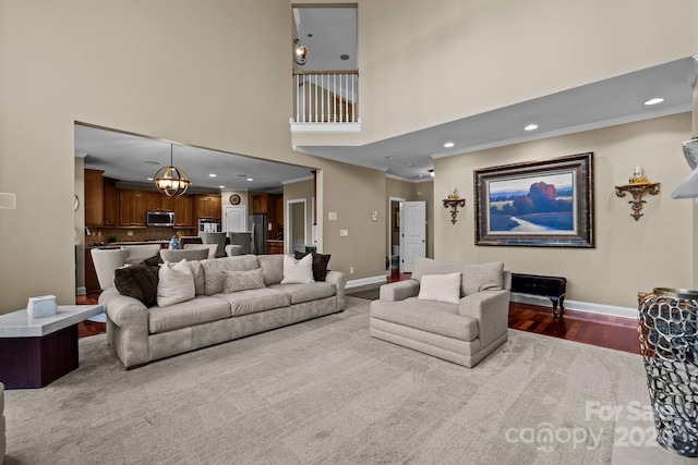 living room with crown molding, light hardwood / wood-style floors, a high ceiling, and a notable chandelier