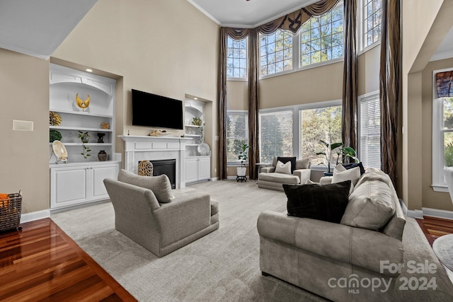 living room with built in shelves, crown molding, wood-type flooring, and a high ceiling