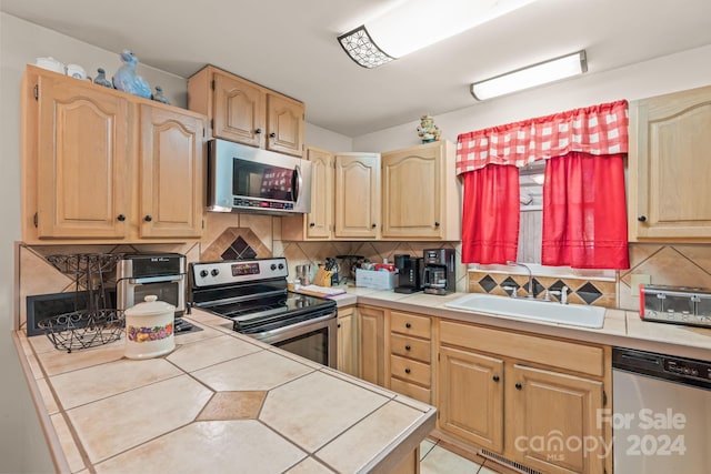 kitchen with tile countertops, sink, backsplash, and appliances with stainless steel finishes