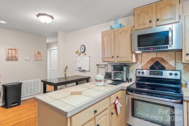 kitchen featuring stainless steel appliances, backsplash, light brown cabinetry, tile countertops, and light hardwood / wood-style flooring