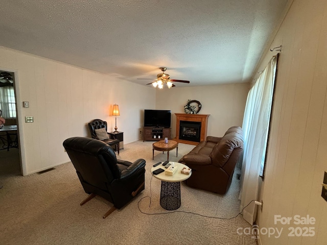 carpeted living room with ceiling fan, a textured ceiling, and wood walls