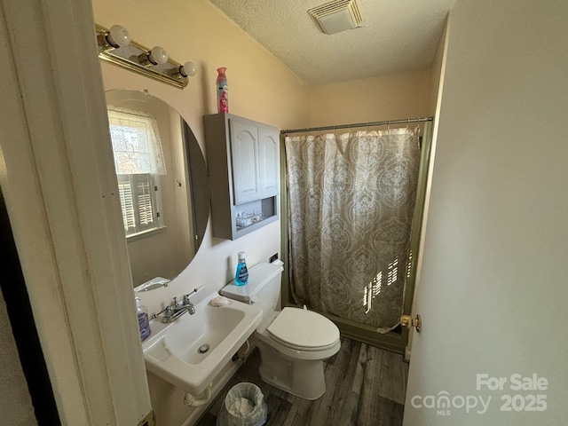 bathroom featuring toilet, sink, hardwood / wood-style flooring, a textured ceiling, and curtained shower