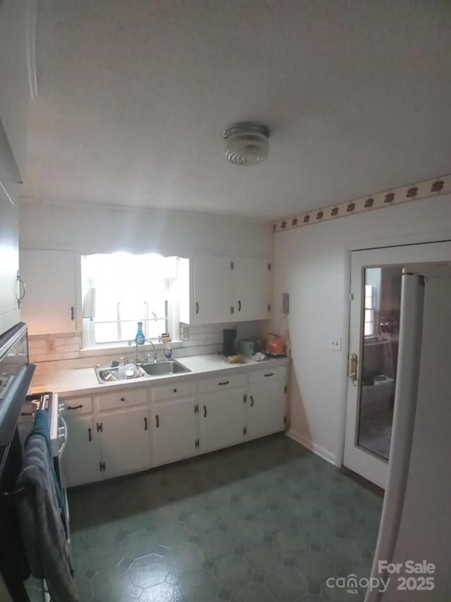 kitchen with decorative backsplash, sink, white cabinetry, and fridge