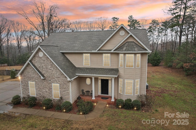 craftsman-style home with a shingled roof, a front yard, stone siding, and driveway