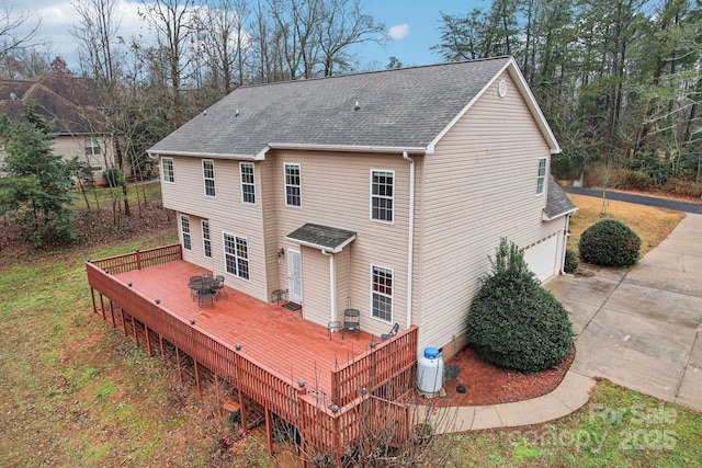 rear view of property featuring an attached garage, a deck, concrete driveway, and roof with shingles
