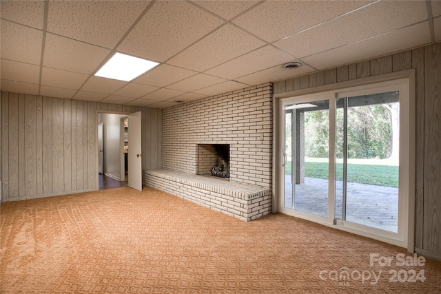 unfurnished living room with a paneled ceiling, wooden walls, light carpet, and a fireplace